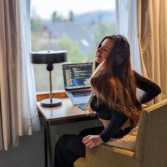 a woman sitting in front of a laptop computer on top of a desk next to a window