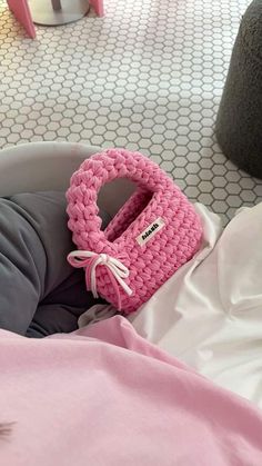 a pink crocheted purse sitting on top of a bed next to a pillow