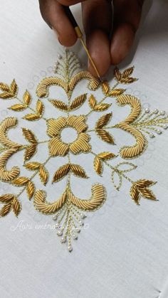 someone is working on an embroidered design with gold thread