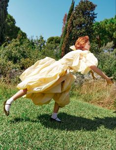 a woman in a yellow dress is dancing on the grass