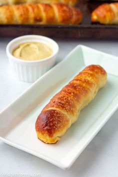 a white plate topped with a pastry next to a bowl of mustard and breadsticks