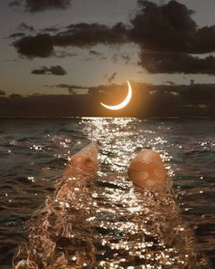 the sun is setting over the ocean with someone's feet submerged in the water