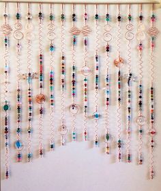 a wall hanging with many different colored beads and chains on it's side in front of a white wall