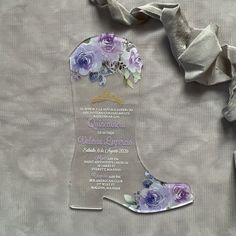 a purple and white wedding card with flowers on the bottom is next to a ribbon