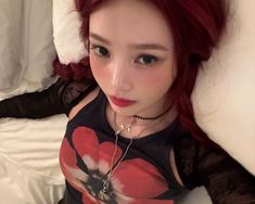 a woman with red hair laying on a bed wearing a black shirt and silver necklace