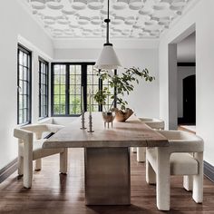 a dining room table with chairs and a potted plant on top of it in front of large windows