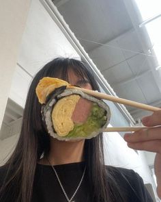 a woman holding a piece of sushi with chopsticks in front of her face