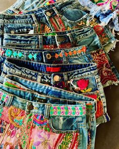 several pairs of jean shorts are stacked on top of each other, all with different colored patches and designs