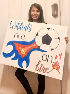 a girl holding up a sign that says wildcats are on fire with a soccer ball