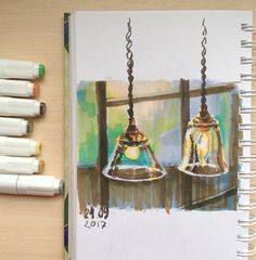 a drawing of two hanging lights on a table next to some markers and pencils