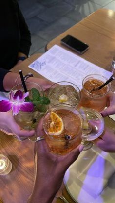 four people holding up glasses with drinks in them on a table at a restaurant or bar