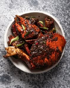 a white bowl filled with meat covered in sauce and garnishes on top of a table