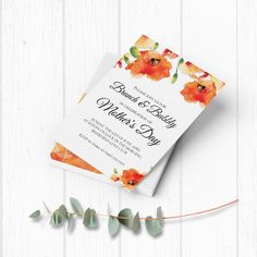 an orange and white floral wedding card on top of a wooden table with greenery