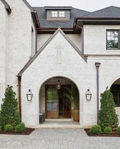 a large white brick house with an arched doorway and two lamps on either side of the entrance