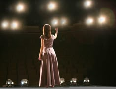 a woman in a long dress standing on stage with her hand up to the sky