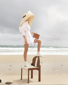 a woman standing on top of a chair near the ocean with her legs in the air