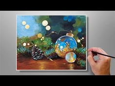 a person is holding a paintbrush and painting a christmas ornament on a canvas