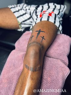 a man with a cross tattoo on his leg sitting in front of a pink towel