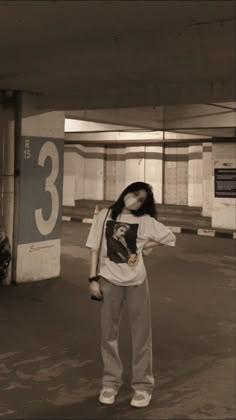 a woman standing in an empty parking garage with her hand on her hip and wearing a mask