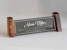 an office name sign is shown on a wooden stand with a black background and white lettering that reads, adam miller office manager