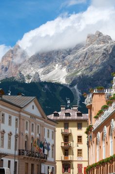 some buildings and mountains in the background with clouds rolling over them on a sunny day