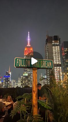 a street sign that says follow and dream in front of a cityscape at night