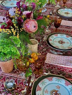 the table is set with plates and vases filled with colorful flowers, greenery, and candles