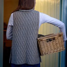 a woman carrying a wicker basket in front of a door with her back to the camera