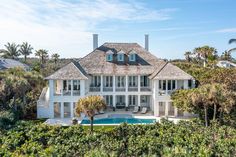 an aerial view of a large white house surrounded by palm trees and greenery with a swimming pool in the foreground