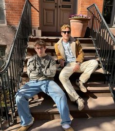 two young men sitting on the steps of a house, one is wearing sunglasses and the other has his arms crossed