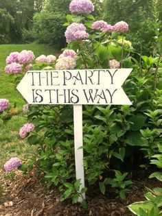 a sign that says the party is this way in front of some bushes and flowers