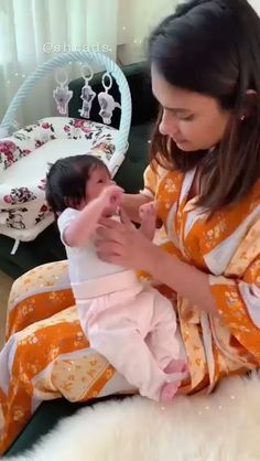 a woman holding a baby in her arms while sitting on top of a white rug