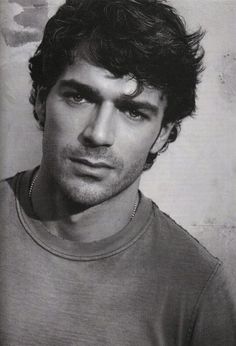 a black and white photo of a man with curly hair wearing a t - shirt