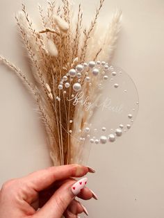 a woman's hand holding a fake flower with pearls on the stems and some white flowers