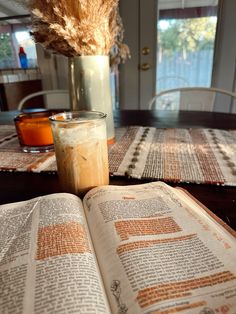 an open book sitting on top of a wooden table next to a glass filled with liquid