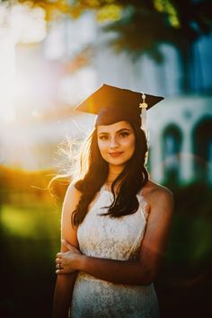 a woman wearing a graduation cap and gown standing in front of a building with her arms crossed