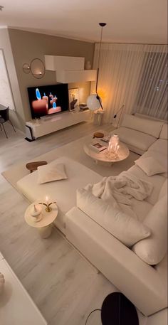 a living room filled with white furniture and a flat screen tv mounted on the wall