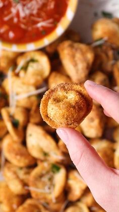 a hand holding up a small fried item in front of some dipping sauce on the side