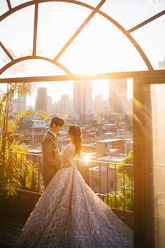 a bride and groom standing on a balcony in front of the city skyline at sunset