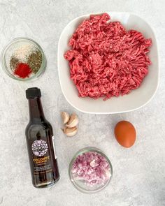 ingredients to make hamburger patties laid out on a counter top, including onions, garlic and an egg