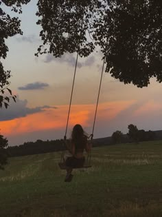 a woman sitting on a swing in the middle of a field as the sun sets