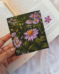 a hand holding an open book with flowers on the cover and in front of it