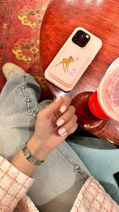 a woman sitting at a table with her cell phone on top of her hand and a drink in front of her