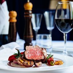 a white plate topped with meat and veggies next to two glasses of wine