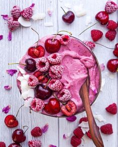 a bowl filled with ice cream and cherries on top of a white table next to fresh raspberries