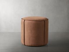 a round stool with a leather cover on it's legs, sitting in front of a gray wall