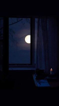 a candle is lit in front of a window with the moon shining through it and trees outside