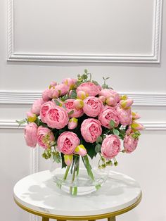 a vase filled with pink flowers sitting on top of a white table next to a wall