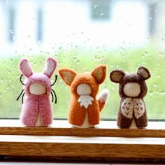 three little stuffed animals sitting on a window sill in front of a rainy window