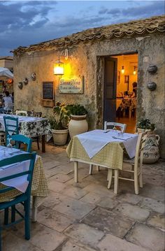 an outdoor dining area with tables, chairs and umbrellas at dusk in front of a stone building